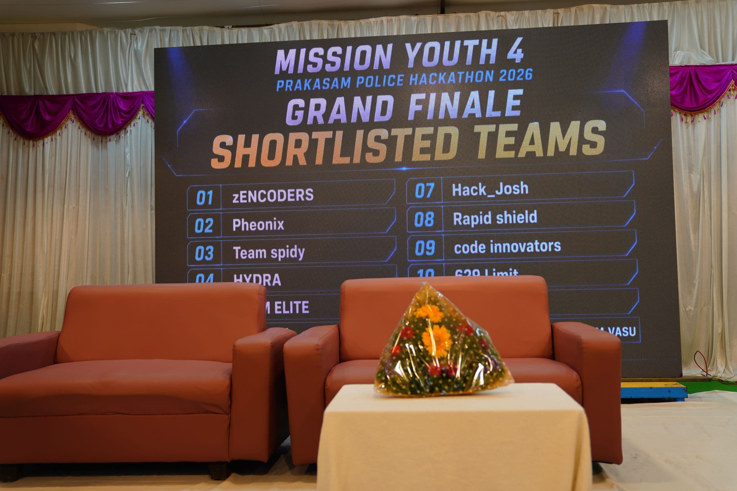 Live leaderboard screen showing the Mission Youth 4 Grand Finale shortlisted teams, with the judges' seating area in the foreground